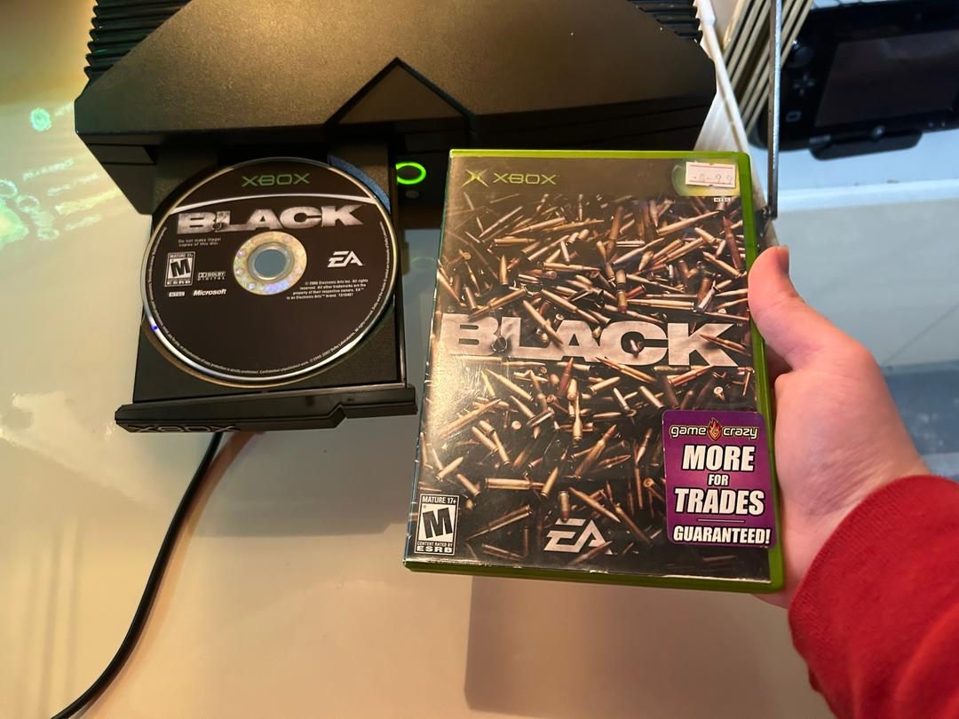 An Xbox with a game called Black in its open disc tray